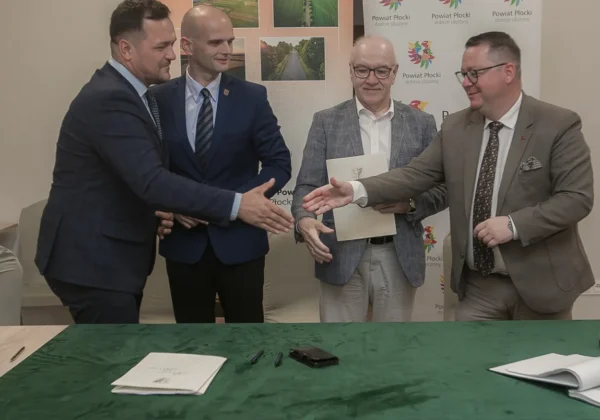 Czterech mężczyzn w garniturach podpisuje umowę na rozbudowę drogi powiatowej Wilkanowo‑Gródkowo, z banerami Powiatu Płockiego w tle.