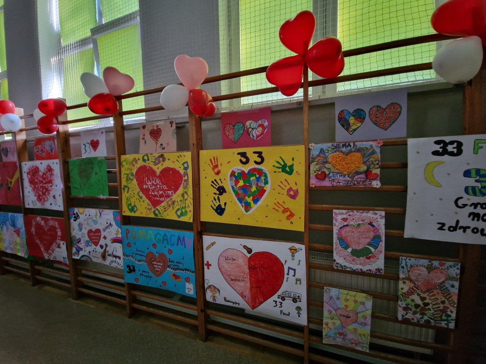 Plakaty dzieci wiszące na drabinkach nawiązujące do WOŚP