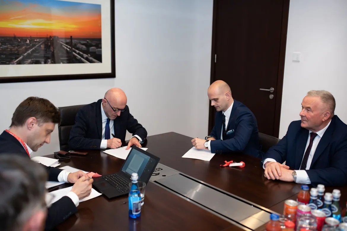 Czterech mężczyzn w garniturach podpisuje dokumenty przy stole konferencyjnym w biurze, co wiąże się z planem Orlenu na przeznaczenie ponad 140 mln zł na drogi powiatowe i gminne.