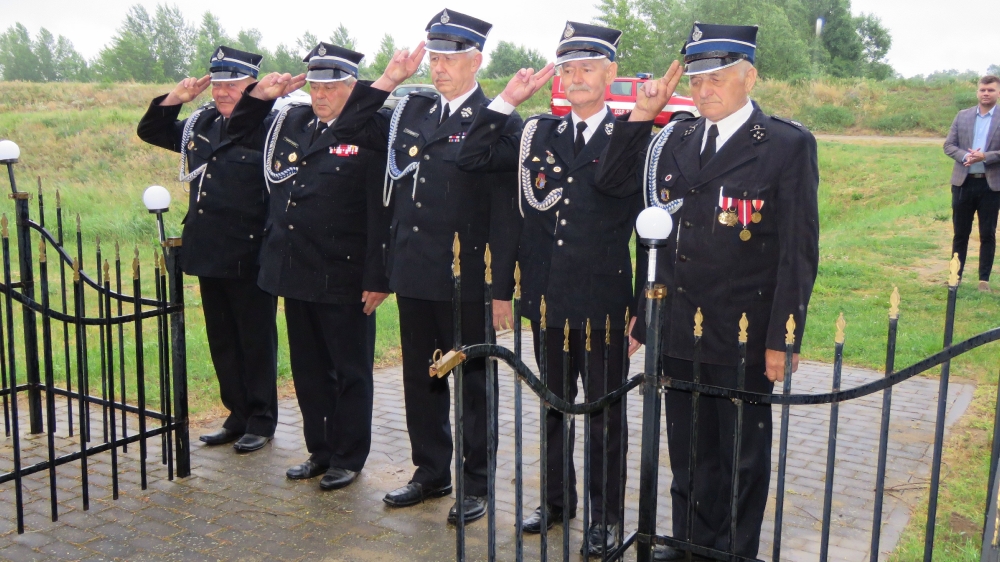 Druhowie OSP salutujący pod kapliczką