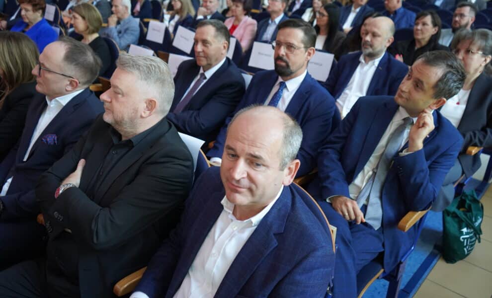 Zdjęcie przedstawia grupę osób siedzących na widowni podczas wydarzenia, skupionych na mówcy lub prezentacji, wśród których widać zarówno mężczyzn, jak i kobiety w formalnych strojach.