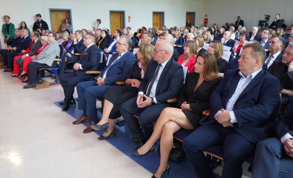 Na zdjęciu przedstawiona jest zgromadzona grupa osób, głównie w eleganckich strojach, słuchająca wystąpienia podczas wydarzenia w sali.