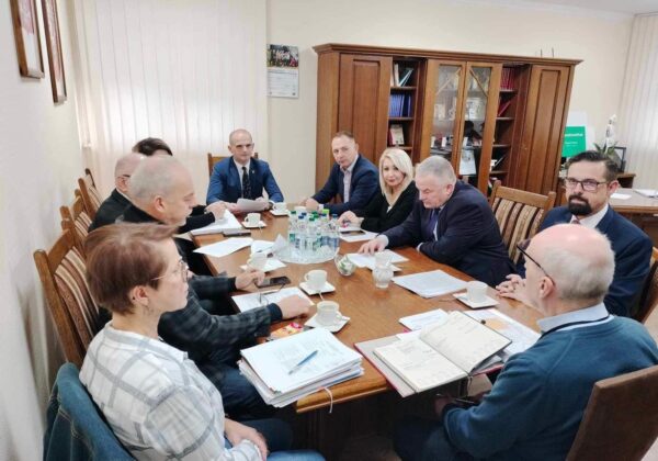 Zebranie grupy osób przy stole w sali konferencyjnej, z dokumentami i filiżankami kawy.