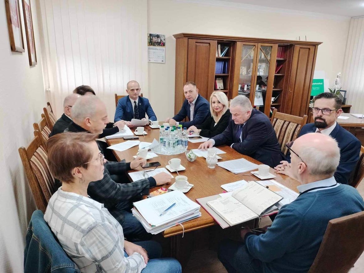 Zebranie grupy osób przy stole w sali konferencyjnej, z dokumentami i filiżankami kawy.