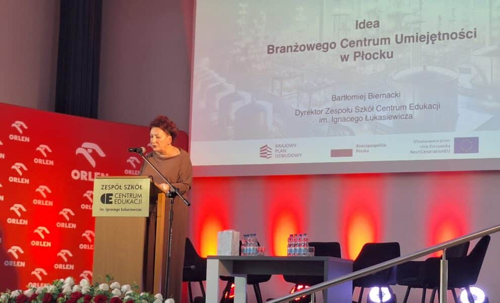 Na zdjęciu Małgorzata Struzik Dyrektor Wydziału Edukacji, Kultury i Spraw Społecznych Starostwa Powiatowego w Płocku przemawiającą na konferencji w Zespole Szkół Centrum Edukacji im. Ignacego Łukasiewicza, z tłem ozdobionym logiem Orlen.