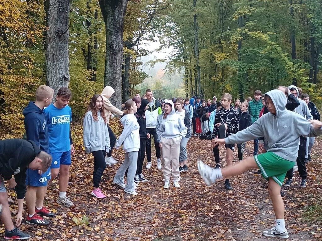 Grupa młodzieży ćwiczy na świeżym powietrzu w otoczeniu kolorowych jesiennych drzew.