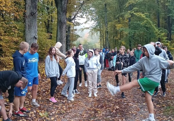 Grupa młodzieży ćwiczy na świeżym powietrzu w otoczeniu kolorowych jesiennych drzew.