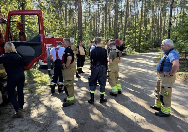 Grupa ratowników w mundurach omawia szczegóły po udanej akcji poszukiwawczej grzybiarza w lesie