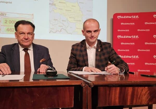 Na zdjęciu widoczna jest dwójka mężczyzn siedzących przy stole, obok nich znajdują się dokumenty oraz gadżet biurowy, a w tle prezentacja z mapą i logo Mazowsza.