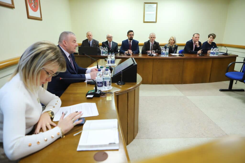 Na zdjęciu widać grupę osób podczas spotkania w sali konferencyjnej, z jednym prelegentem mówiącym do reszty uczestników siedzących przy stole.