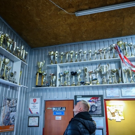 Na zdjęciu widać mężczyznę oglądającego kolekcję pucharów i trofeów na półkach w pomieszczeniu.