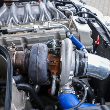 Na zdjęciu znajduje się silnik samochodowy z turbosprężarką oraz widocznymi przewodami i elementami mechanicznymi.