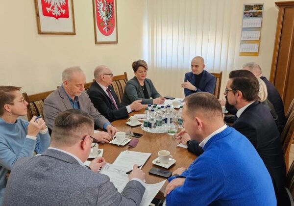 Na zdjęciu widoczna jest grupa osób siedzących przy stole w sali konferencyjnej, prowadzących dyskusję oraz analizujących dokumenty.