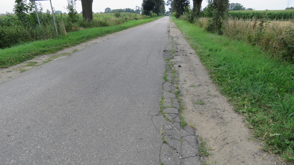 Droga wiejska w Orszymowie z widocznymi uszkodzeniami, otoczona zielenią, planowana do remontu.