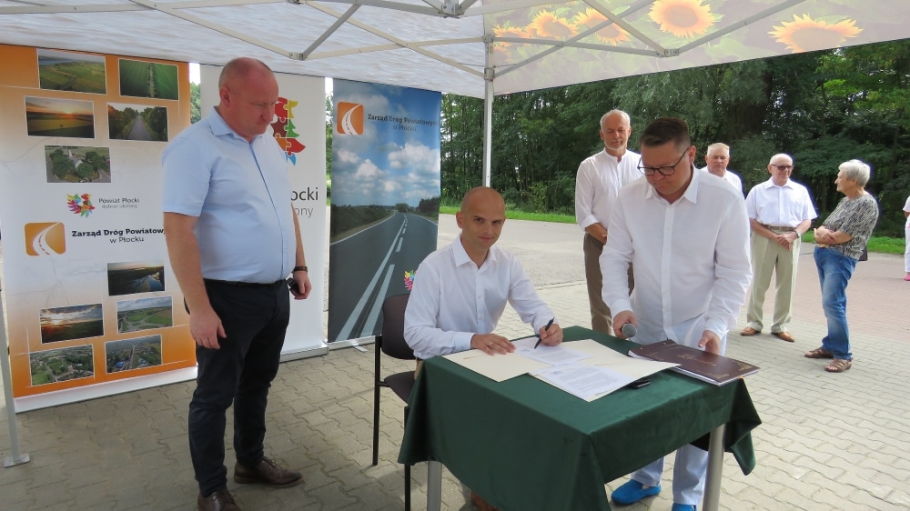 Na zdjęciu widać podpisanie umowy dotyczącej remontu drogi w Orszymowie, z uczestnikami ceremonii w tle.