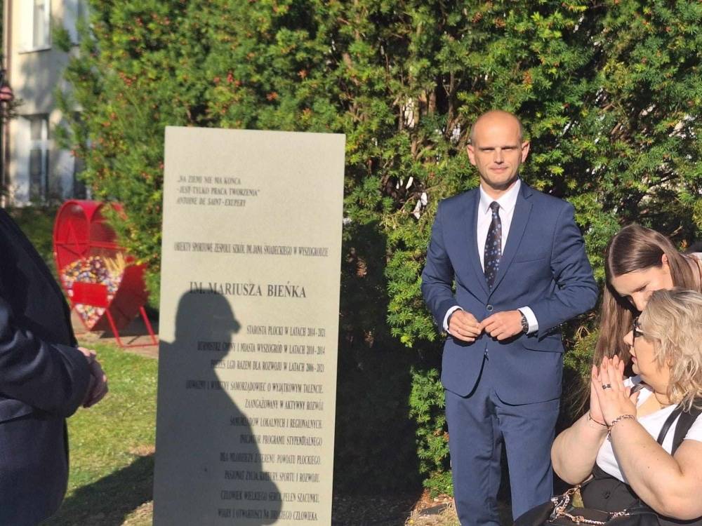 Na zdjęciu widoczna jest uroczystość związaną z nadaniem imienia Mariusza Bieńka szkole w Wyszogrodzie, podczas której obecni są uczestnicy i pomnik z inscription.