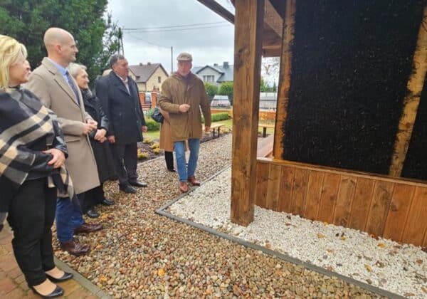 Grupa osób z zainteresowaniem ogląda nową konstrukcję w przyjaznym otoczeniu, w deszczowy dzień.