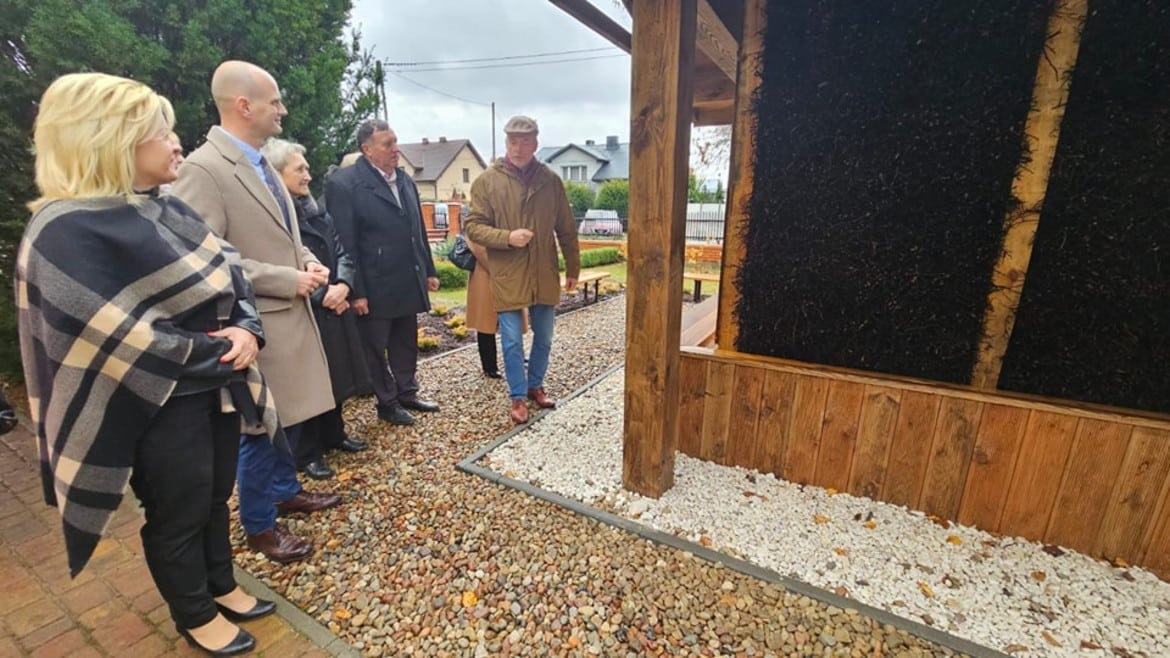 Grupa osób z zainteresowaniem ogląda nową konstrukcję w przyjaznym otoczeniu, w deszczowy dzień.