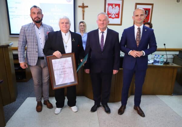 Na zdjęciu czterech mężczyzn stoi obok siebie w sali obrad, trzymając wyróżnienie dla Andrzeja Szymona Kulińskiego.