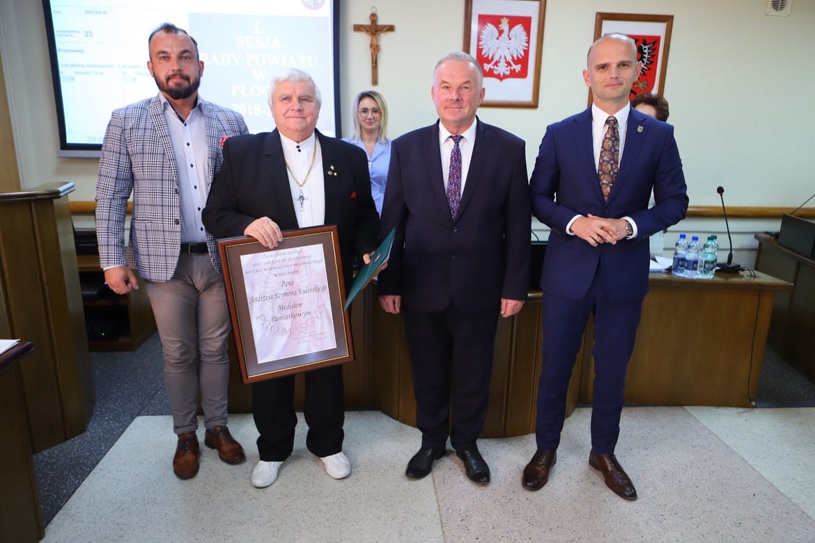Na zdjęciu czterech mężczyzn stoi obok siebie w sali obrad, trzymając wyróżnienie dla Andrzeja Szymona Kulińskiego.
