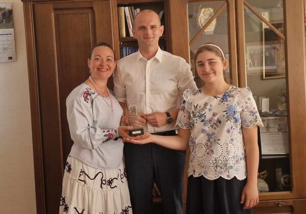 Trzy osoby, w tym mężczyzna i dwie kobiety, uśmiechają się, trzymając podziwiany puchar w domowym wnętrzu.