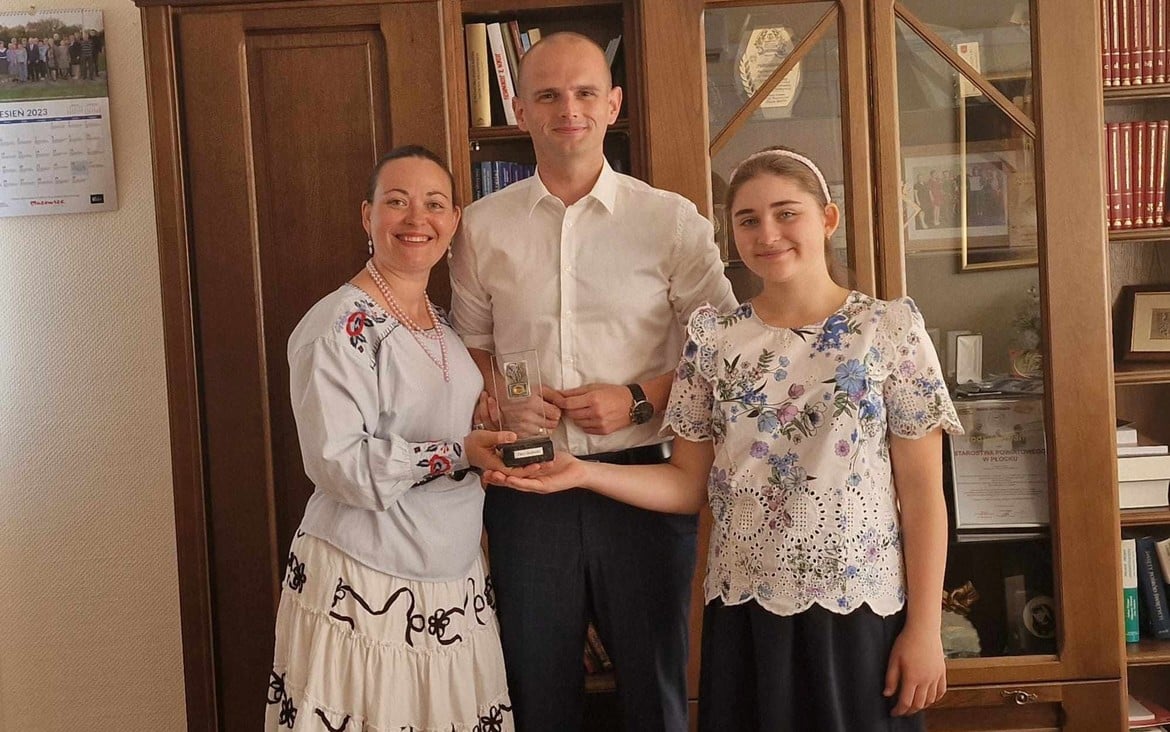 Trzy osoby, w tym mężczyzna i dwie kobiety, uśmiechają się, trzymając podziwiany puchar w domowym wnętrzu.