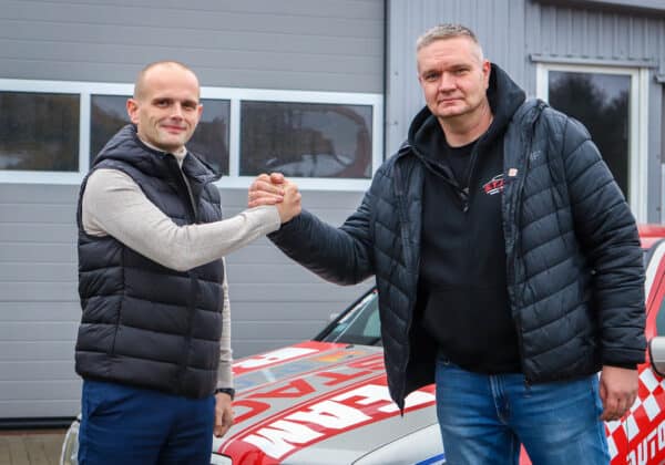 Na zdjęciu dwóch mężczyzn uścisnęło sobie ręce na tle samochodu i szarej budynku.