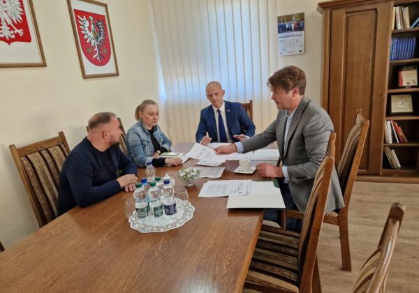 Na zdjęciu widać cztery osoby siedzące przy stole w biurze, gdzie prowadzą rozmowę i przeglądają dokumenty.