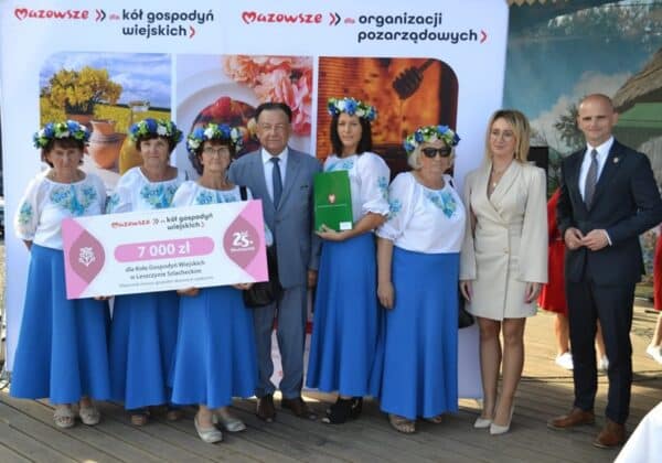 Na zdjęciu widoczne są członkinie Koła Gospodyń Wiejskich z Leszczycy Szlacheckiej, które otrzymują czek na 7000 zł, stojąc w towarzystwie lokalnych przedstawicieli.