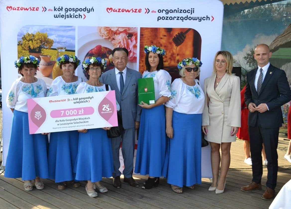 Na zdjęciu widoczne są członkinie Koła Gospodyń Wiejskich z Leszczycy Szlacheckiej, które otrzymują czek na 7000 zł, stojąc w towarzystwie lokalnych przedstawicieli.