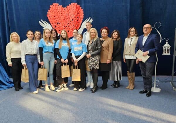 Zdjęcie przedstawia grupę osób pozujących na tle serca wykonanego z papierowych serc, w ramach wydarzenia społecznego.