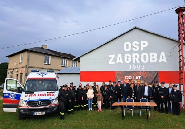 Na zdjęciu widoczna jest grupa ludzi, w tym przedstawiciele straży pożarnej, zgromadzona przed budynkiem OSP Zagroba z okazji 120-lecia tej jednostki.