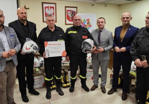 Zdjęcie przedstawia grupę mężczyzn, w tym strażaków, którzy otrzymują hełmy i certyfikat z okazji przekazania wsparcia dla miejscowości Nowa Góra.