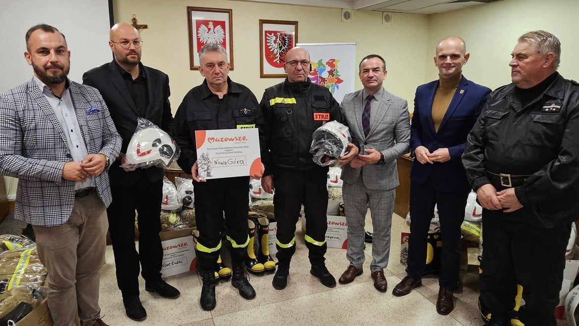 Zdjęcie przedstawia grupę mężczyzn, w tym strażaków, którzy otrzymują hełmy i certyfikat z okazji przekazania wsparcia dla miejscowości Nowa Góra.
