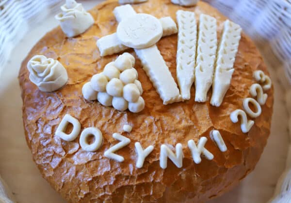 Chleb dożynkowy ozdobiony ornamentami w postaci krzyża, kłosów, winogron oraz napisu "Dożynki 2023".