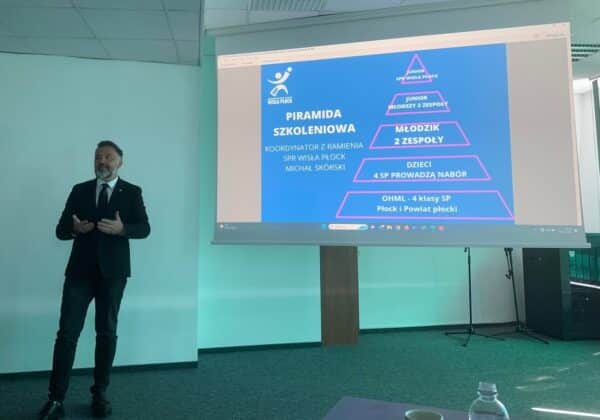 Na zdjęciu widać mężczyznę w garniturze prezentującego piramidę szkoleniową na tle ekranu z informacjami o programie szkoleniowym SPR Wisła Płock.