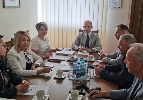 Na zdjęciu widać grupę osób w formalnej atmosferze spotkania przy stole, z dokumentami i napojami.