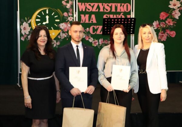 Na zdjęciu przedstawione są cztery osoby, które uczestniczą w uroczystości wręczenia dyplomów, stojąc na scenie przed kolorowym tłem z kwiatami i napisem „WSZYSTKO MA SWÓJ CZAS”.