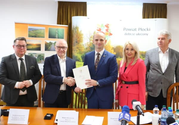 Na zdjęciu przedstawiono grupę osób podczas uroczystego wręczenia dokumentu w biurze Powiatu Płockiego.