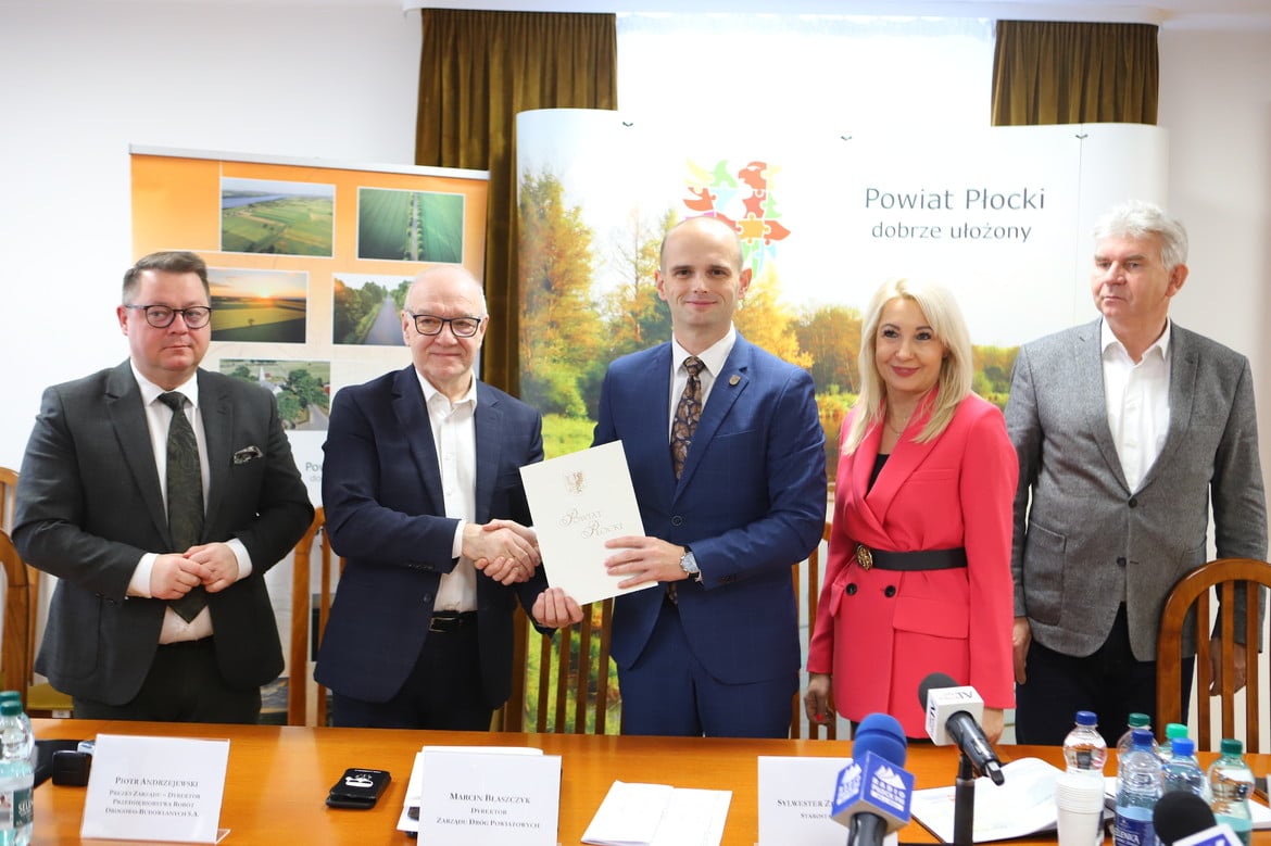 Na zdjęciu przedstawiono grupę osób podczas uroczystego wręczenia dokumentu w biurze Powiatu Płockiego.