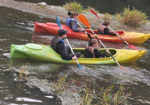Na zdjęciu widoczni są uczestnicy spływu kajakowego w kolorowych kajakach na wodnym szlaku.