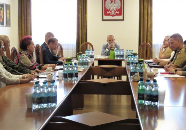 Na zdjęciu widoczna jest grupa osób siedzących przy długim stole w sali konferencyjnej, prowadzących dyskusję lub spotkanie.