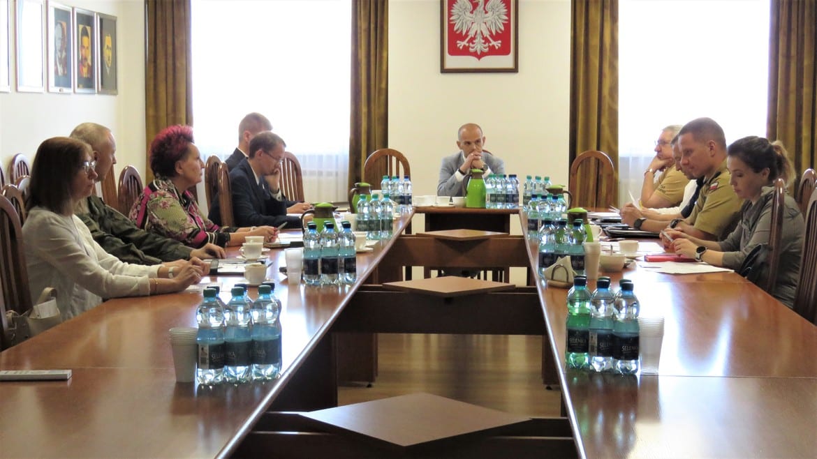 Na zdjęciu widoczna jest grupa osób siedzących przy długim stole w sali konferencyjnej, prowadzących dyskusję lub spotkanie.