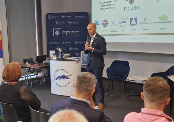 Zdjęcie przedstawia mężczyznę przemawiającego podczas spotkania w Izbie Gospodarczej Regionu Płockiego, z widokiem na uczestników konferencji.