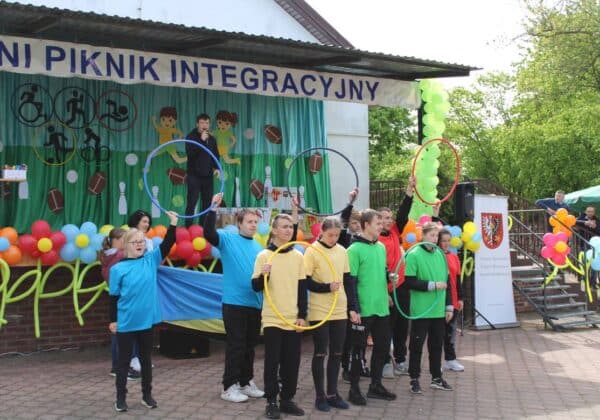 Na zdjęciu widoczna jest grupa młodzieży w kolorowych koszulkach, prezentująca występ w trakcie wydarzenia pod hasłem "Integracyjny Piknik".