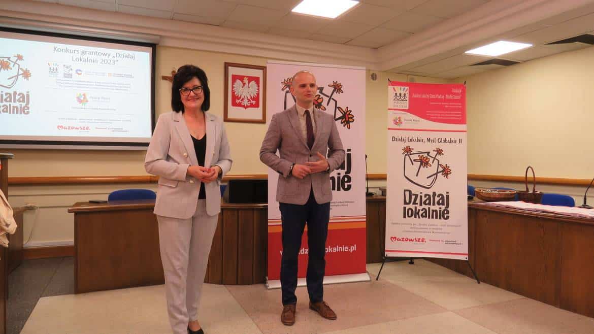 Na zdjęciu widać dwóch prelegentów podczas wydarzenia dotyczącego konkursu grantowego "Działaj Lokalnie 2023", stojących przed banerami promującymi inicjatywę.