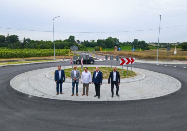 Na zdjęciu widać grupę pięciu mężczyzn stojących na rondzie, z zielonymi terenami w tle.