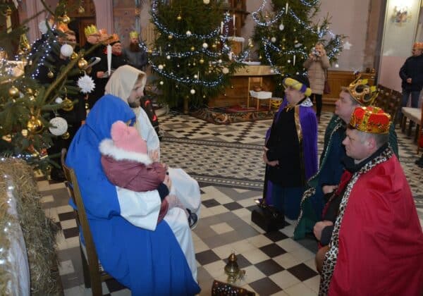 Scena przedstawia postać Marii z Dzieciątkiem Jezus w otoczeniu trzech mędrców oraz dekoracji choinkowych, w przedświątecznej atmosferze w kościele.