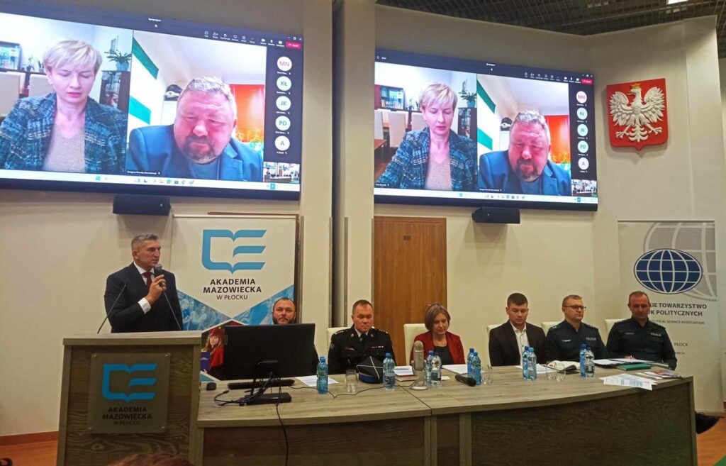 Zdjęcie przedstawia spotkanie w Akademii Mazowieckiej w Płocku, z osobami uczestniczącymi zarówno na żywo, jak i zdalnie, które omawiają ważne tematy.