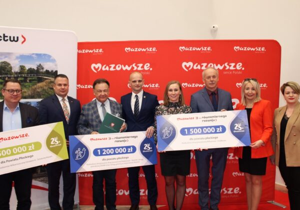 Na zdjęciu grupa osób stoi z dużymi czekami przedstawiającymi przyznane fundusze dla powiatu płockiego, w tle widoczne logo Mazowsza.